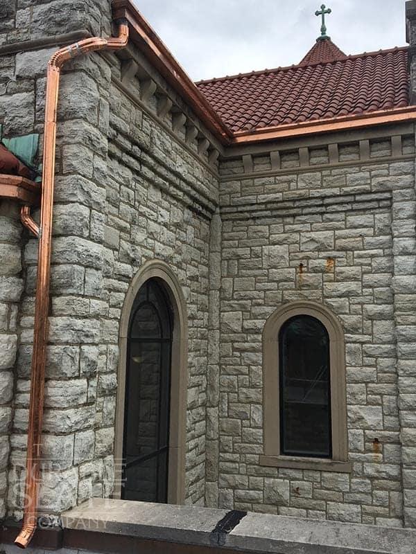 copper gutter and downspout, with a stone wall and red clay tile roof