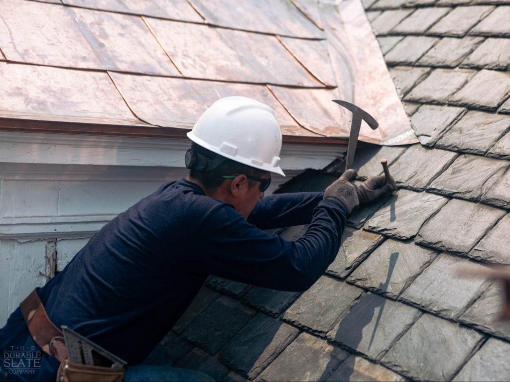 durable slate employee repairing a slate roof with a traditional hammer